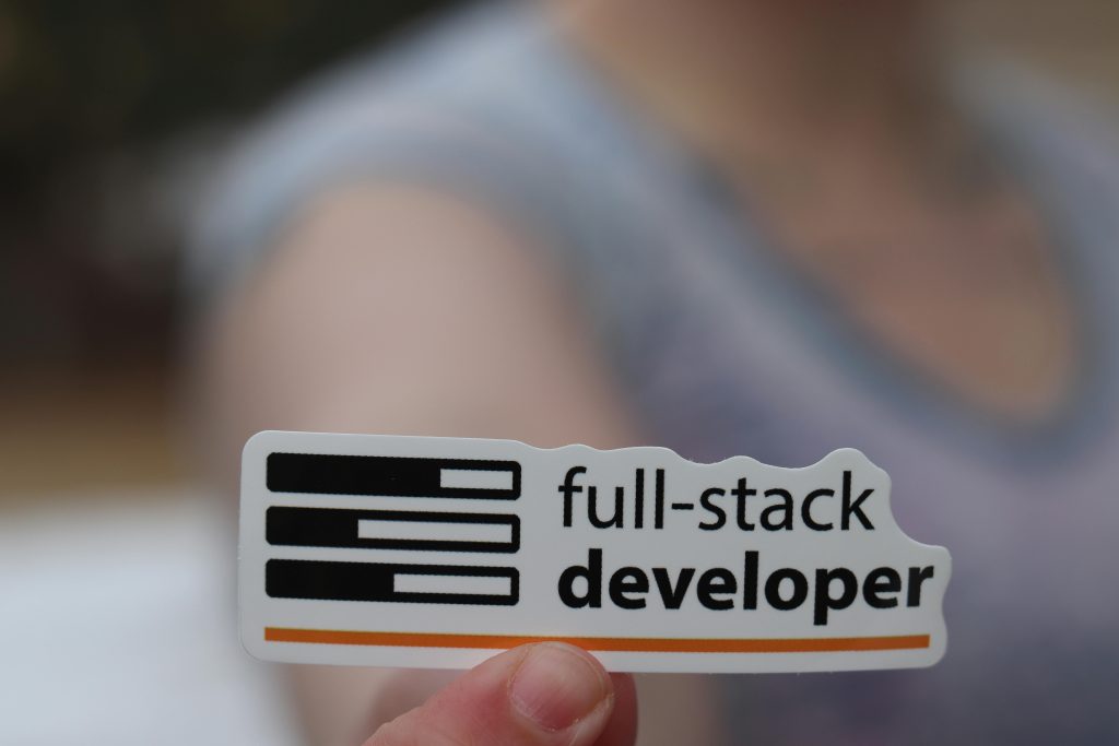 A hand holding a sticker labeled 'full-stack developer', symbolizing technology and programming skills.